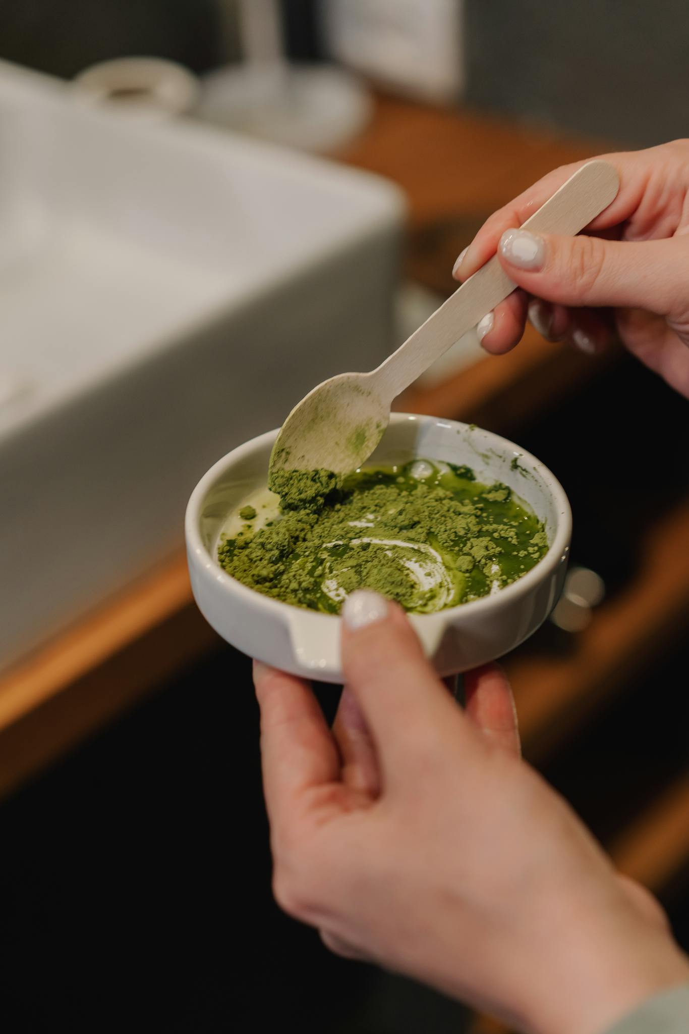 Close-up of a woman blending a green skincare mask in a stylish indoor setting.