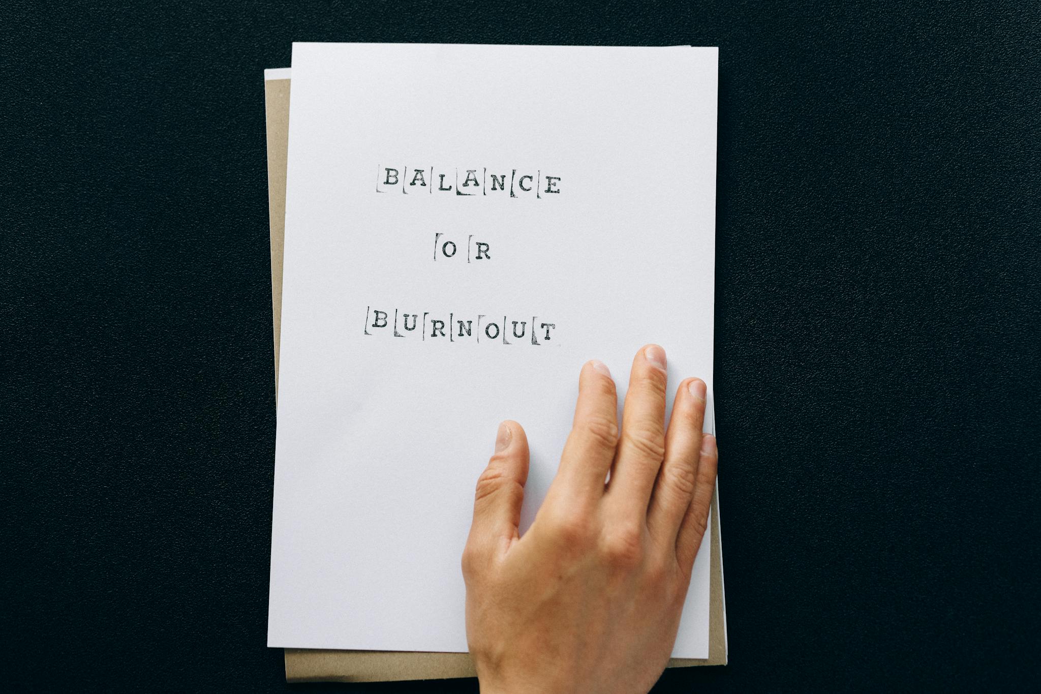 Hand holding paper with 'Balance or Burnout' text, promoting mental wellness.